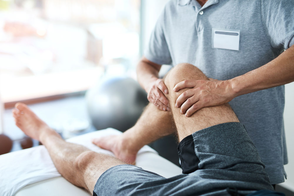 Man's injured knee being treated by a physical therapist.